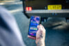 A hand holding a smartphone with the ARK Smart Connector app controlling trailer lights; the trailer’s rear and number plate are visible in the background.