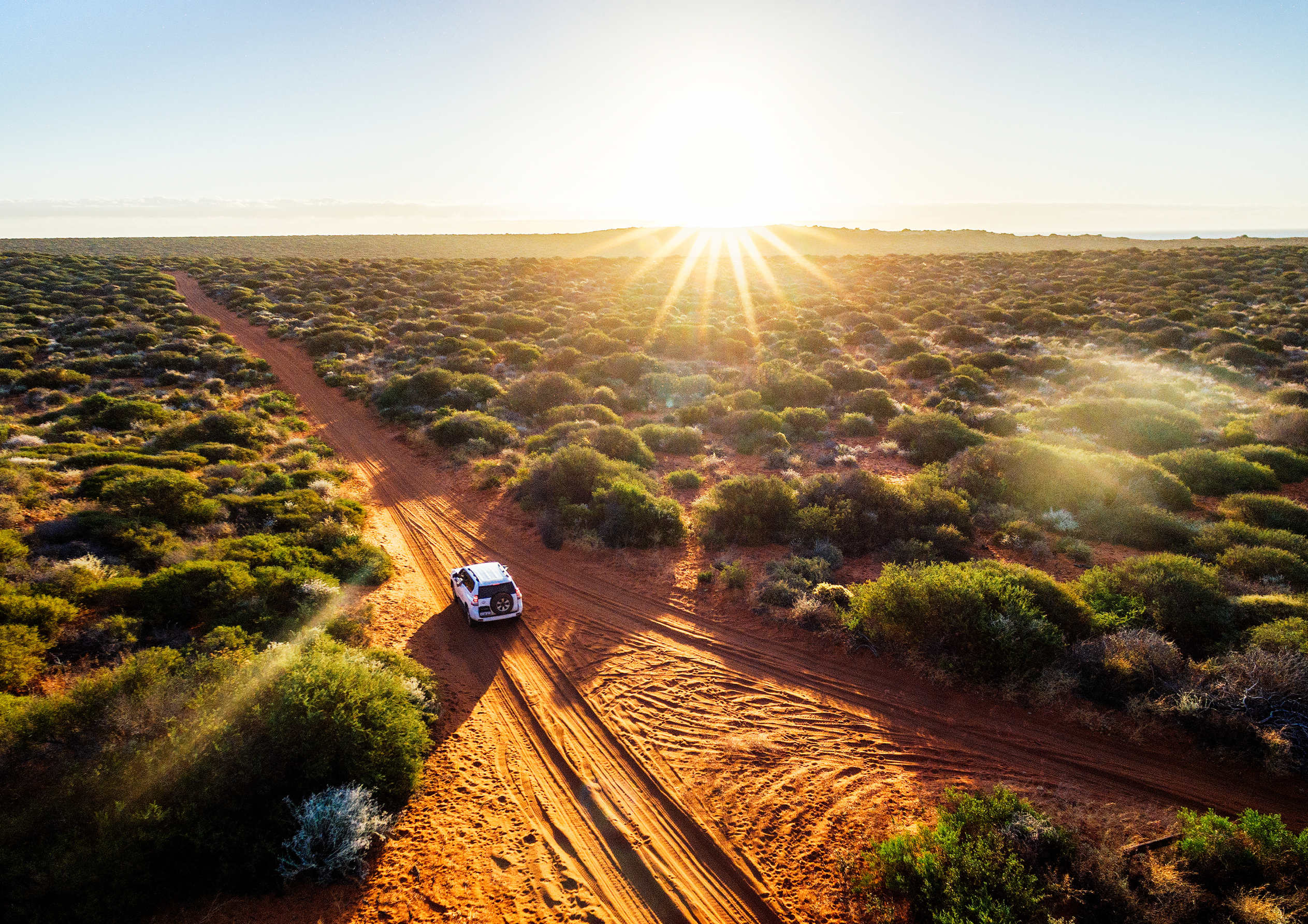 4WD vehicle driving along a dirt road at sunrise