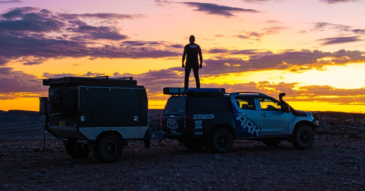 Man standing on top of truck near trailer at sunset in outback