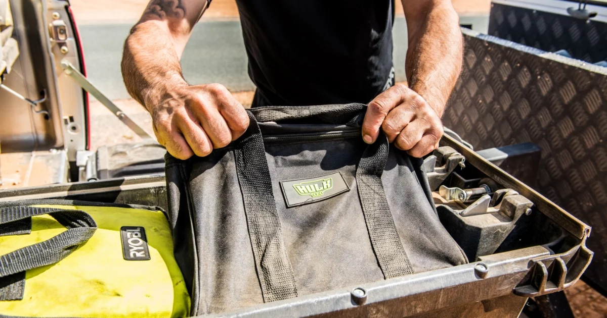 Man grabbing a black kit bag from a truck bed