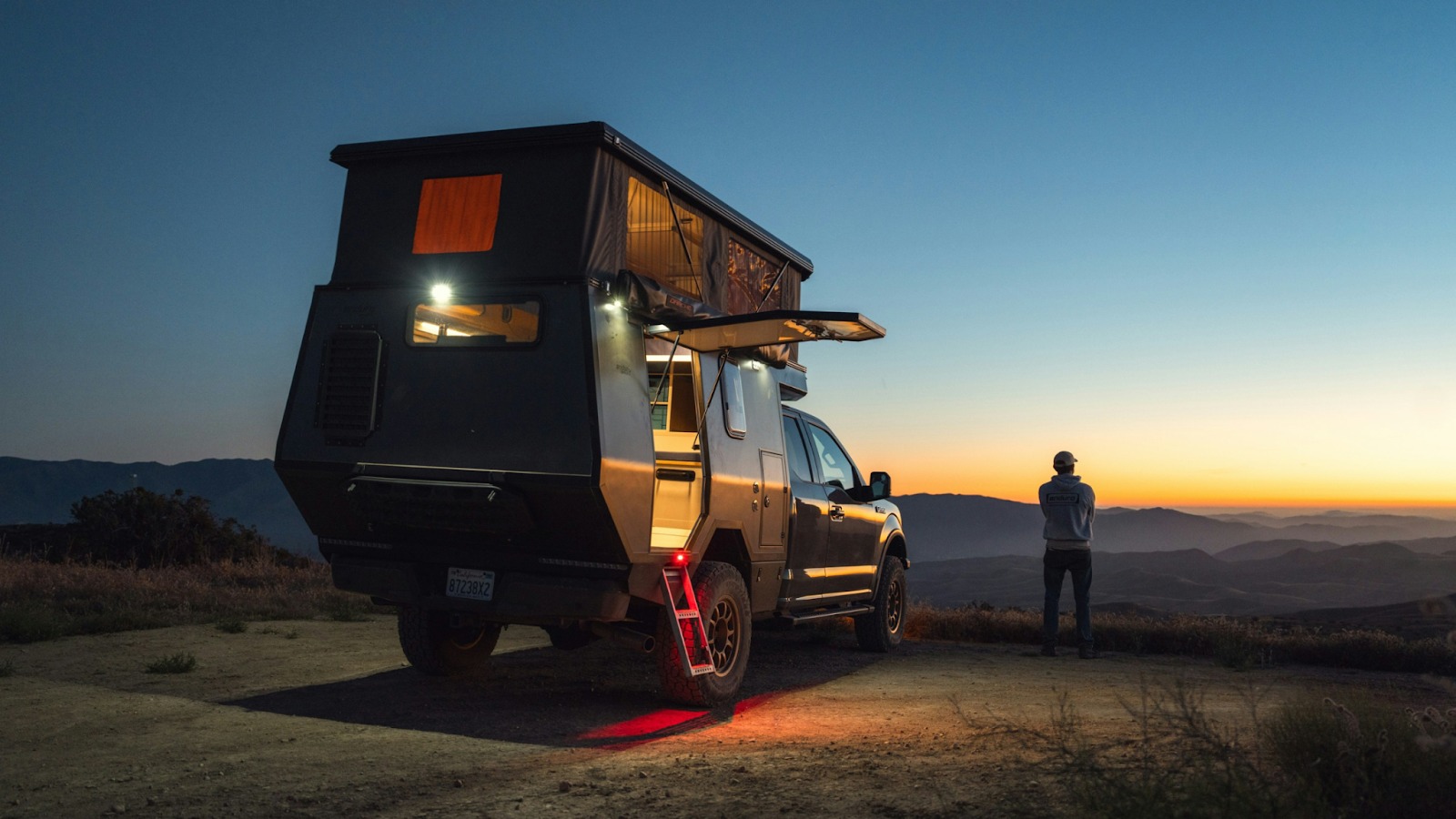 A man standing next to his 12V powered off-grid set up at sunset