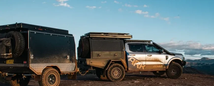ARK 4WD towing an off-road camper trailer on a rugged track overlooking mountain views.