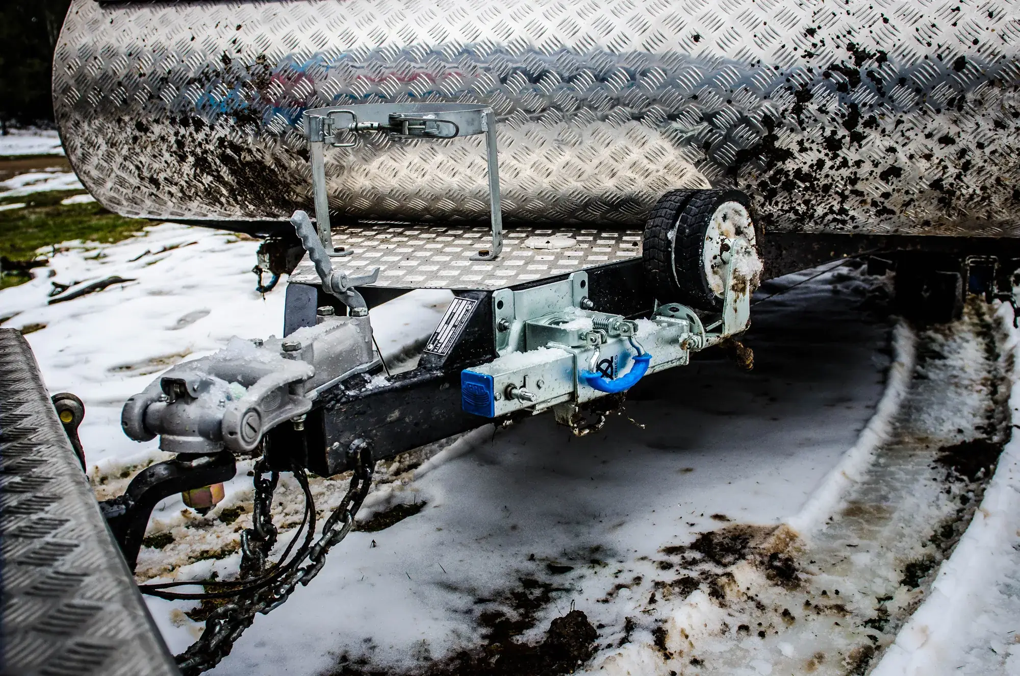 Boat trailer drawbar, coupling and safety chains in snow, with the trailer wheel behind.