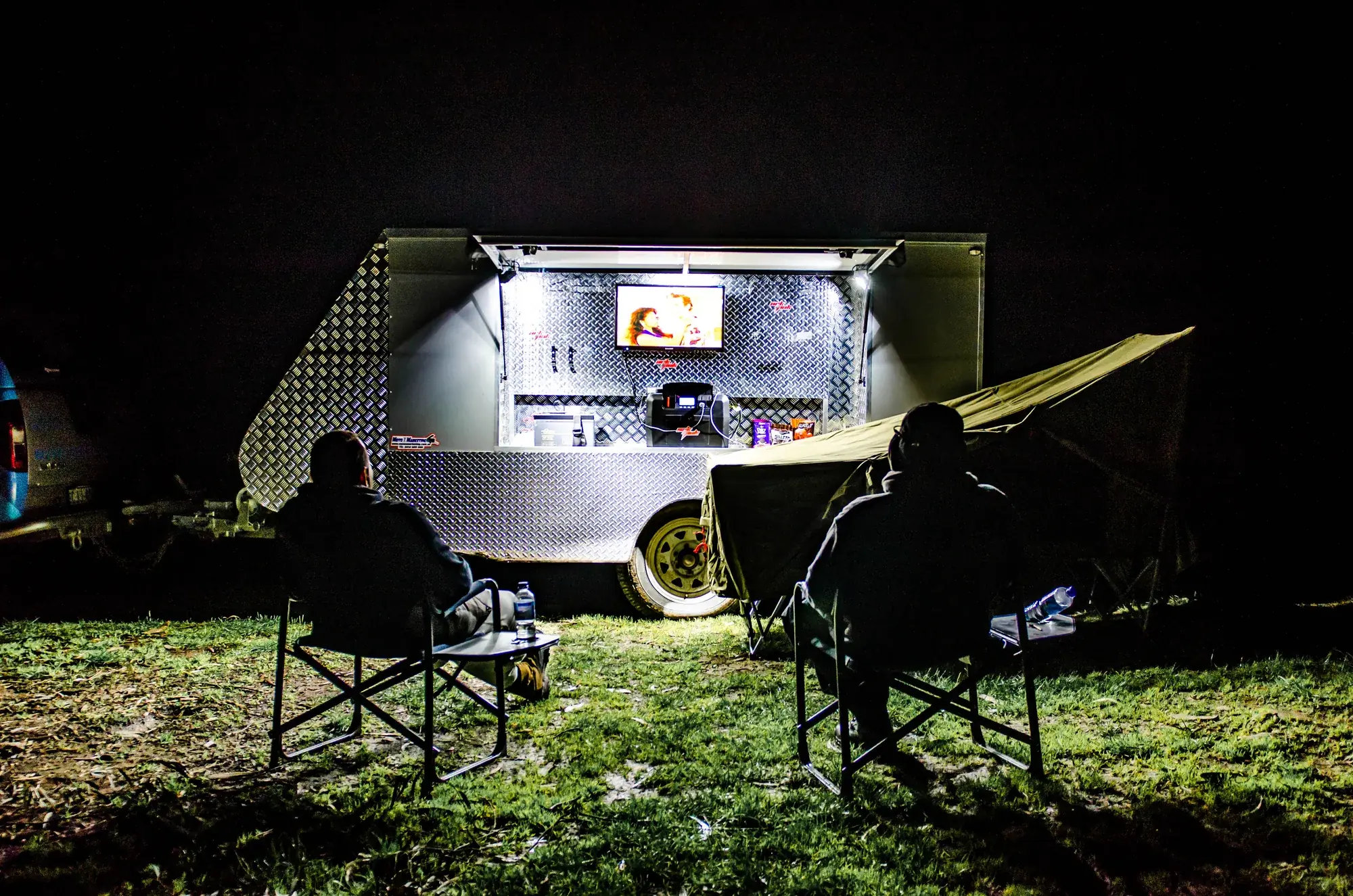 Camper trailer set up at a bush camp at night, with the trailer wheel in frame.